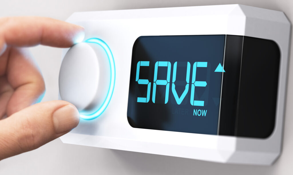 Thermostat with digital display that says "save now" and person's hand turning white knob next to the display.