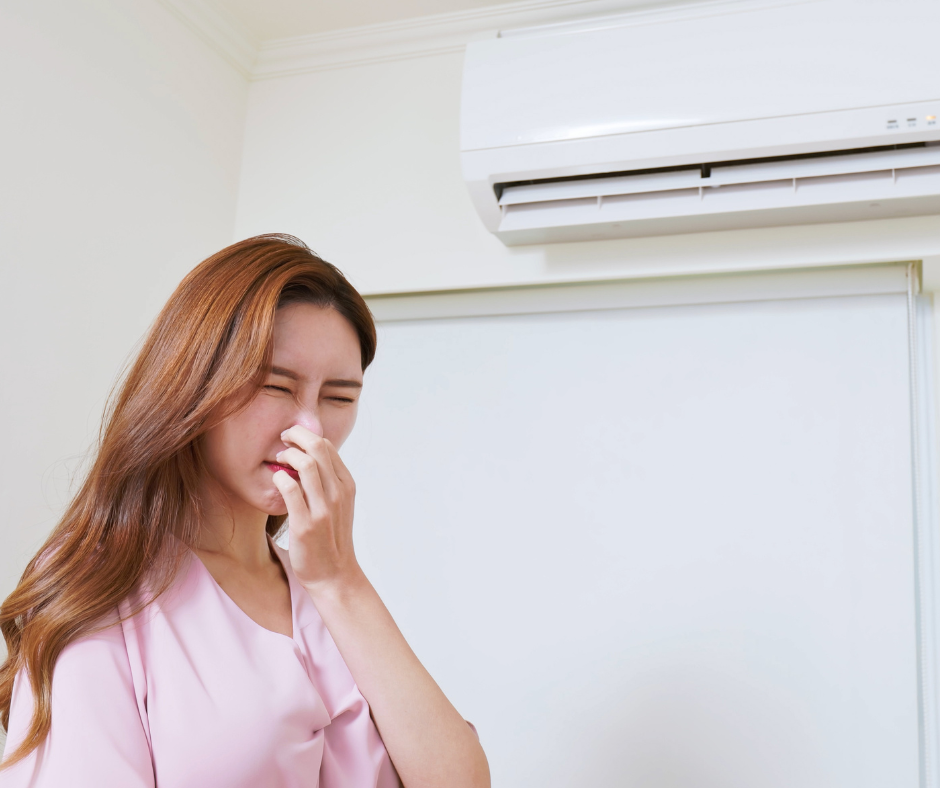 A woman holds her nose while standing in front of a heater