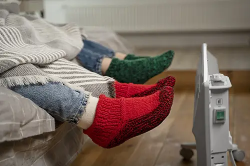 Two people warming feet near space heater—potential sign of furnace not working efficiently in Plano, TX